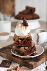Brownie sliced ​​with a scoop of ice cream on top with a piece of chocolate. In the background is a northerly table with milk and the rest of the brownies.