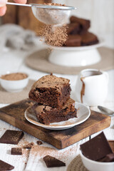Brownie cut into pieces sprinkled with cocoa. There is a nordic table in the background.