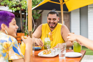 gay man and bisexual woman smiling and enjoying a delicious meal on the terrace of an outdoor restaurant.