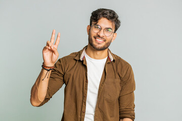 Happy Indian young man showing victory sign, hoping for success and win, doing peace gesture,...