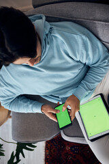 Phone, green screen and a man playing games on a sofa in the living room of his home from above. Tablet, gaming and young gamer using a display or screen with tracking markers for entertainment