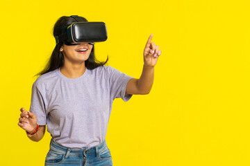 Excited happy Indian young woman using headset helmet app to play simulation game. Watching virtual reality 3D 360 video. Arabian girl in VR goggles isolated on yellow background. Future technology