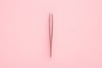 New tweezers on light pink table background. Pastel color. Closeup. Top down view.