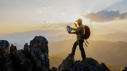 The hiker with a backpack stood on the rock after examining the map to find a path in a beautiful mountain landscape. - obrazy, fototapety, plakaty
