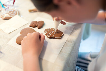 Girl decorating gingerbread cookies with icing sugar. Selective focus.