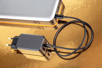 Power bank and charging plug on a golden background. Electronic devices for charging gadgets