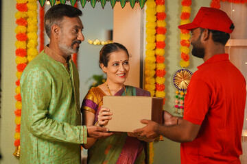 Senior couples receiving parcel or package from delivery person at home door during Diwali festival...