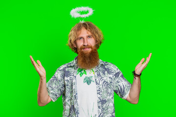 Portrait of smiling shy angelic young caucasian man with angel halo nimb over head flirting, looking at camera, positive love emotions celebrating holiday. Redhead bearded guy on chroma key background