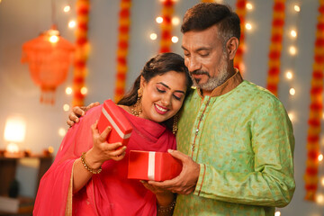 Happy senior father giving surprise gift to daughter at diwali festival celebration at home - concept of special occasion, family festive ceremony and relationship bonding. - Powered by Adobe
