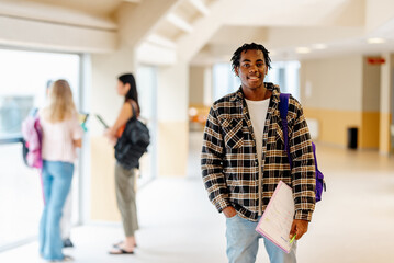 Portrait of a young black man, college student, standing in the campus hallway with notes in his hand. Education, diversity and inclusion
