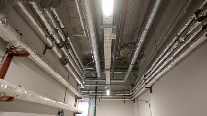 Pipes, ventilation and air conditioning in an underground garage. New house. Pipes in the basement of a new house. New metal pipes in the basement of a residential building.