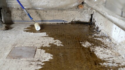 Floor priming process. A worker applies a primer to a concrete floor before laying a self-leveling...