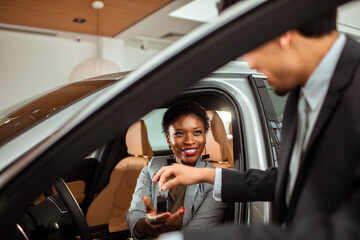 Young African American woman receiving the keys of the car she bought at the dealership