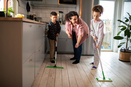 Young mixed mother teaching her kids how to sweep floors at home