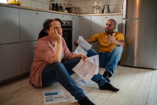 Young mixed couple going over bills and payments together on the floor of the kitchen at their home