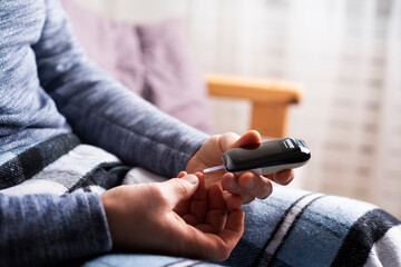Obraz premium Middle age caucasian man sitting on the sofa to measure glucose level by glucose meter