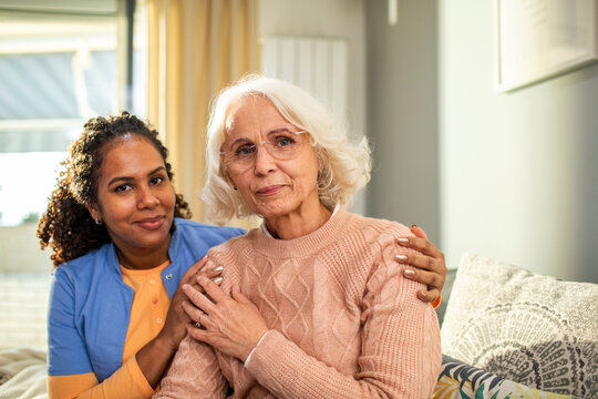 Senior woman and her caregiver looking at the camera in the living room at home