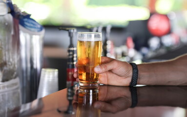 Fototapeta na wymiar Man's hand holds glass of beer on bar. All inclusive in hotels in concept resorts