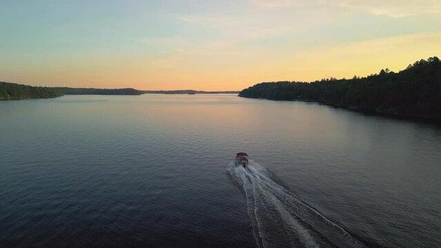 An aerial of a pontoon boat cruising on a lake at sunset