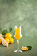 Limoncello in grappas wineglass, sweet Italian lemon liqueur, traditional strong alcoholic drink and lemons on the green wooden background.