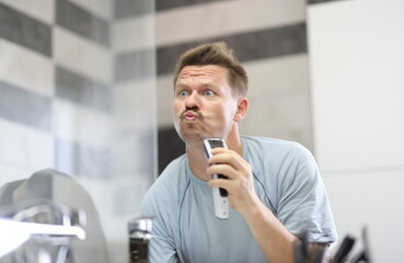 Man in front of a mirror shaves off his stubble with machine. How to properly shave off facial...