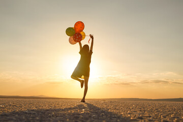 Silhouette of woman holding balloons while standing at beach against sky during sunset