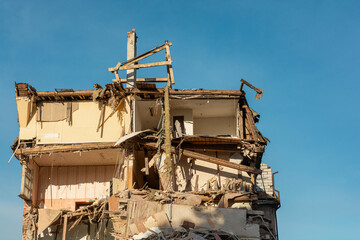 Fototapeta na wymiar Destroyed residental building. Upper floors of destroyed house with broken apartments and a pile of construction debris. Buildings damaged by terrorist attack, war or earthquake
