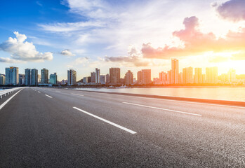 Asphalt road and city skyline with modern buildings at sunset by the sea