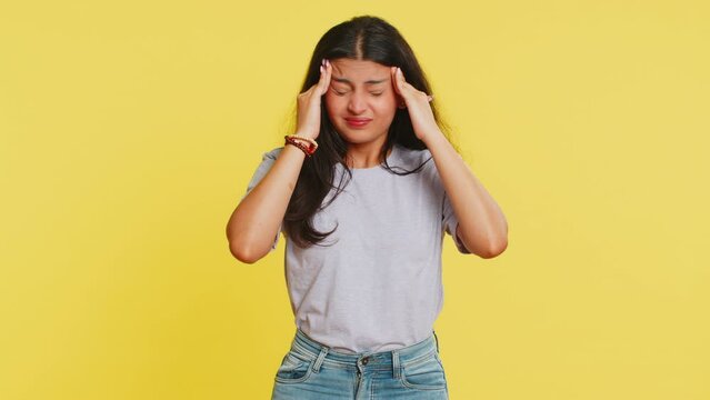 Displeased exhausted Indian Hindu woman girl rubbing temples to cure headache problem, suffering from tension, migraine, stress, grimacing in pain, high blood pressure isolated on yellow background