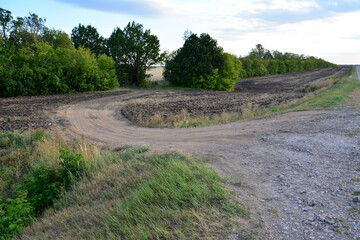 dirty road in the shape of loop with green trees on background in dawn