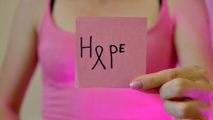 Breast Cancer Awarness Month. Inscription hope on pink streaker in female hand close-up.
