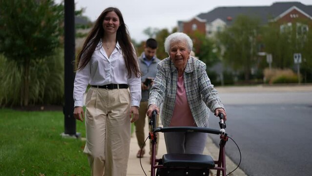 Grandmother using a walker and granddaughter smiling and walking together outside.
