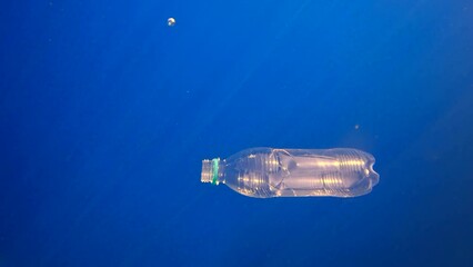 Transparent disposable plastic bottle sinks in blue water slowly sinking to rocky seabed in sunrays, Slow motion, Mediterranean Sea, Greece