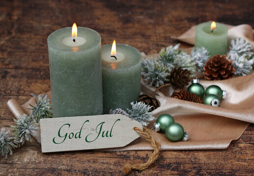 Weihnachtsgrußkarte: Grüne Kerzen mit Weihnachtskugeln und der Beschriftung God Jul auf einem Schild.