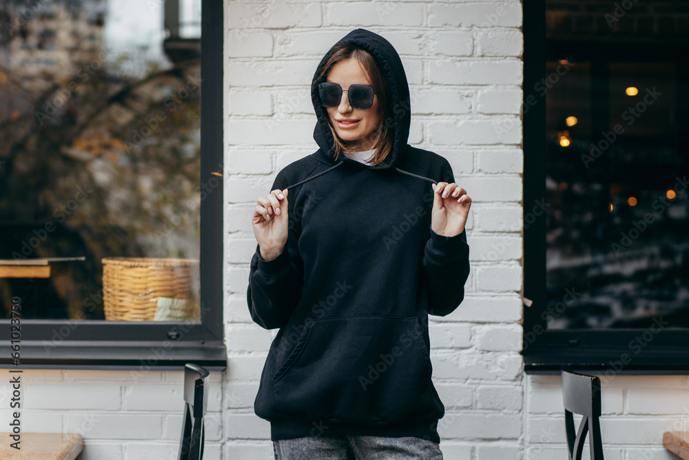 Wall mural Young woman in glasses and black hoodie