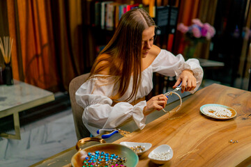a young beautiful girl makes jewelry with her own hands cuts the remnants of wire for a necklace...