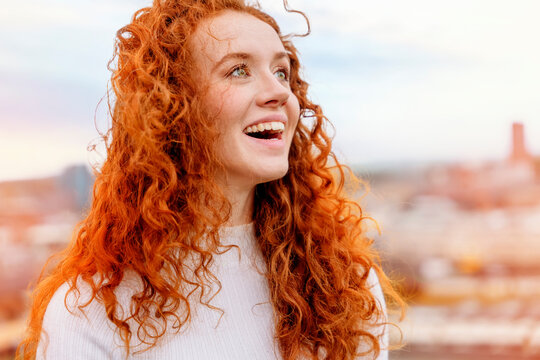 delighted readhead female model laughs happily enjoys spare time taking selfie portrait outside against blurred city background. Lifestyle concept