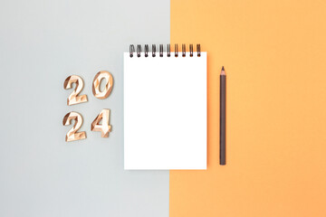 Blank notepad mock up, pencil and 2024 numbers on a blue and gold background. New Year goals list concept.