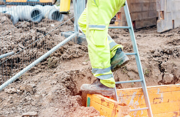 Groundworker builder using steps ladder to get out of the deep drainage eaxcavation trench support...