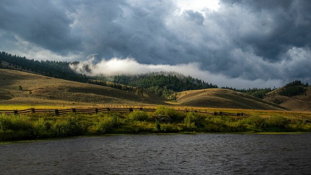 clouds hover over a pasture with a lake on the bank