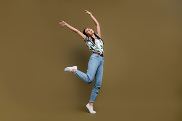 Fototapeta na wymiar Full size portrait of energetic delighted girl stand one leg raise arms closed eyes dancing isolated on brown color background