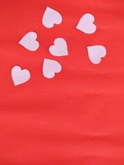 White paper hearts on red paper background for Valentine's Day festival.