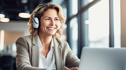 Happy professional mature female hr manager, smiling mature mid aged business woman in office wearing earbud looking at laptop computer having hybrid conference work meeting or remote job interview - obrazy, fototapety, plakaty