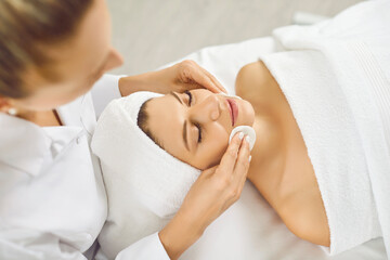 Fototapeta na wymiar Cosmetologist doing skincare treatment for a young pretty woman in spa salon. Portrait of a female client lying in beauty clinic having a face massage and receiving beauty procedure from beautician.