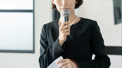 マイクを持って話す喪服姿の女性