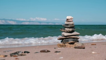 pyramid of stacked stones on the seashore symbolizes balance and harmony in nature. suddenly, pyramid of stones collapses from the incoming wave. concept of imbalance, violation of the balance. - Powered by Adobe