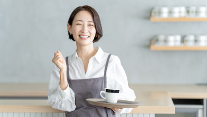 エプロン姿でガッツポーズする女性　カフェ店員