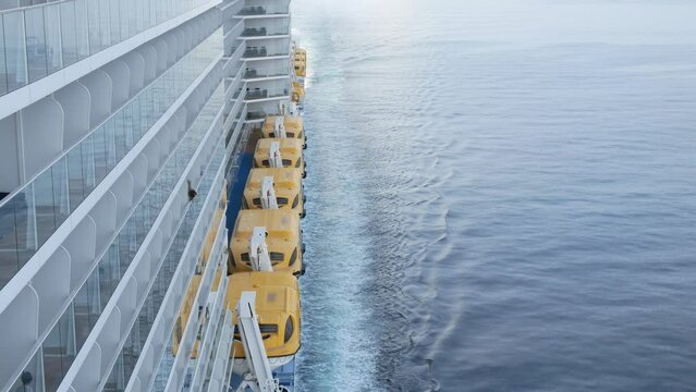 view to the back aft of the cruise ship from front deck area with side view of the passenger cruise ship while cruising in the sea in day time with many lifeboats