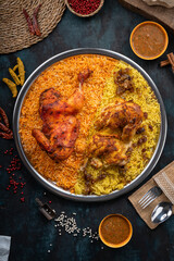 Mandi rice dish with grilled chicken meat and spices on a dark green background