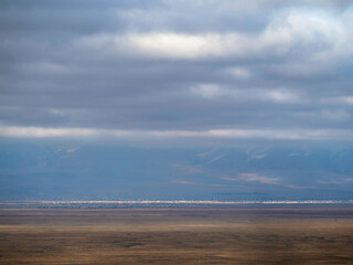 Thin line of a distant city in the steppe under a blue cloudy sky. Altai steppe.